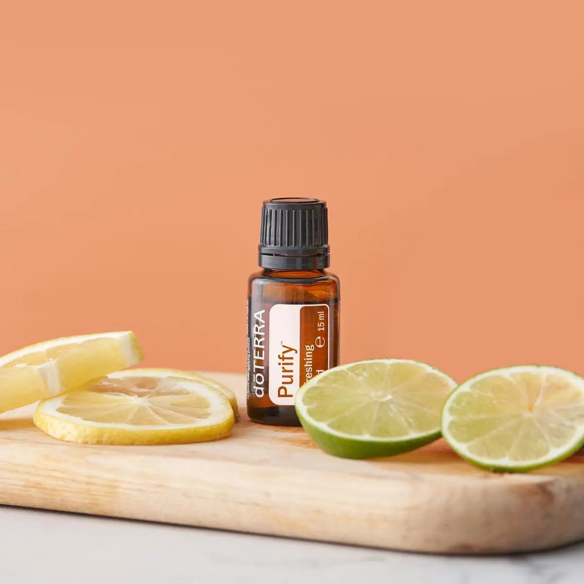 Mezcla dōTERRA Purify 15ml — frasco en tabla de madera con rodajas de limón y lima sobre fondo naranja melocotón