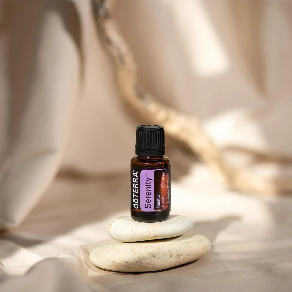 Mezcla dōTERRA Serenity 15ml — frasco junto a piedras zen apiladas con luz cálida y fondo beige