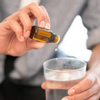 Mezcla dōTERRA Zendocrine 15ml — manos echando una gota en vaso de agua con hielo en primer plano