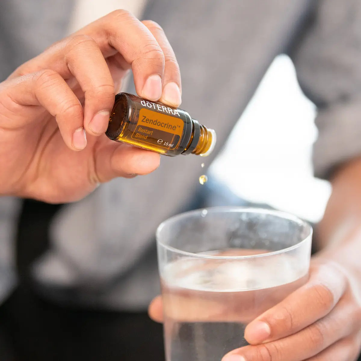 Mezcla dōTERRA Zendocrine 15ml — manos echando una gota en vaso de agua con hielo en primer plano