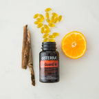 On Guard+ Softgels doTERRA con capsulas doradas derramandose del frasco junto a media naranja y corteza de arbol sobre marmol blanco