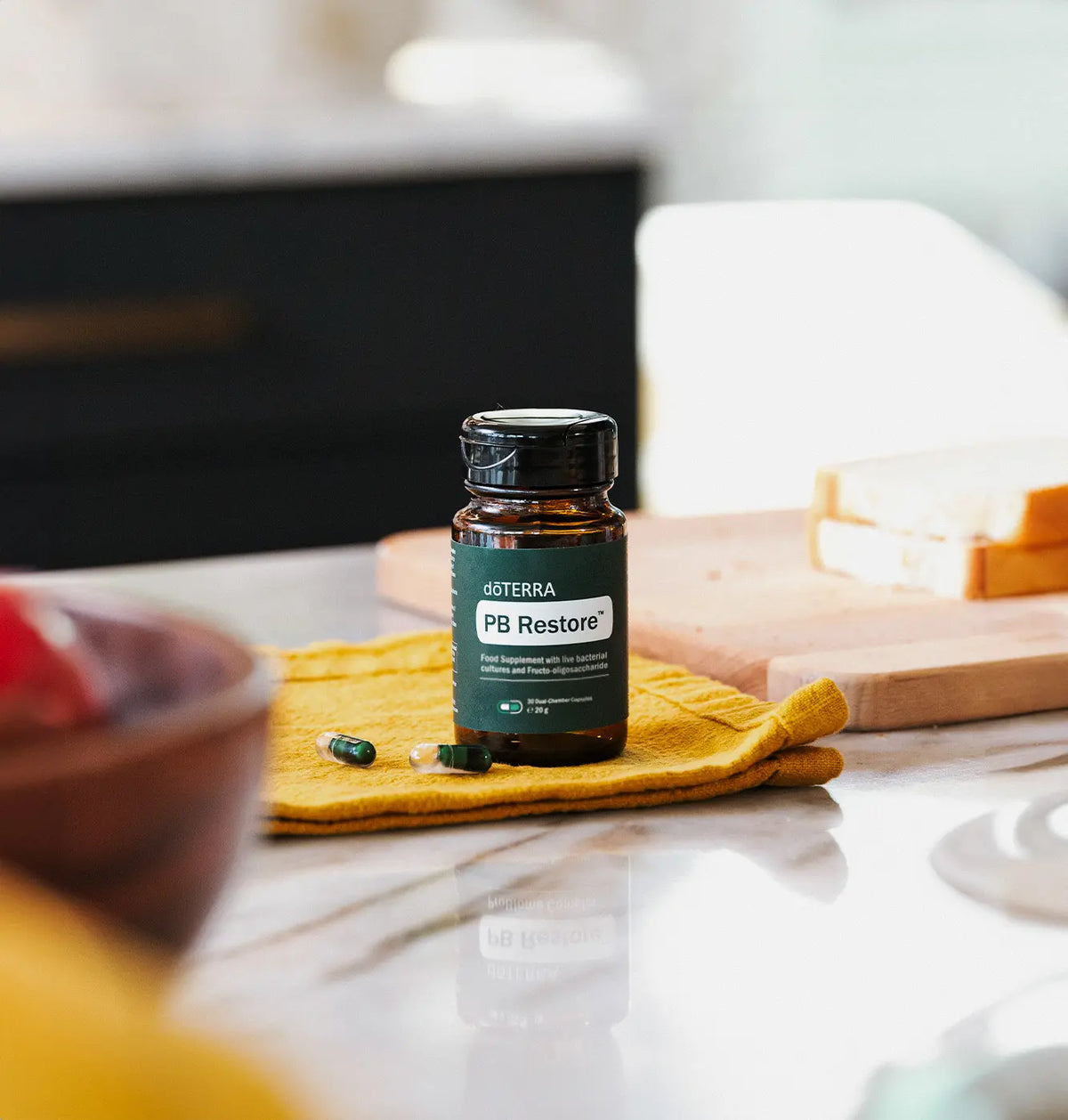 PB Restore doTERRA sobre tela de lino mostaza en encimera de marmol de cocina, con capsulas sueltas y tabla de madera al fondo
