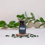 PB Restore doTERRA frasco oscuro sobre rodaja de madera con capsulas bicolor verde y transparente y planta de hojas verdes al fondo