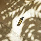 Perlas MetaPWR dōTERRA — frasco en suelo de parque de madera con sombras de árbol y luz solar, vista cenital