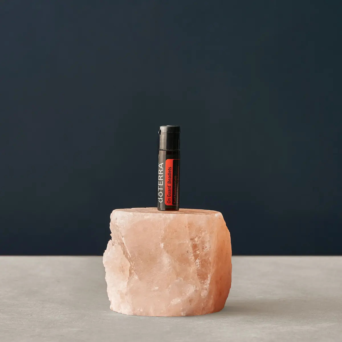 Perlas On Guard dōTERRA — frasco junto a bloque de sal del Himalaya sobre fondo azul pizarra en estudio