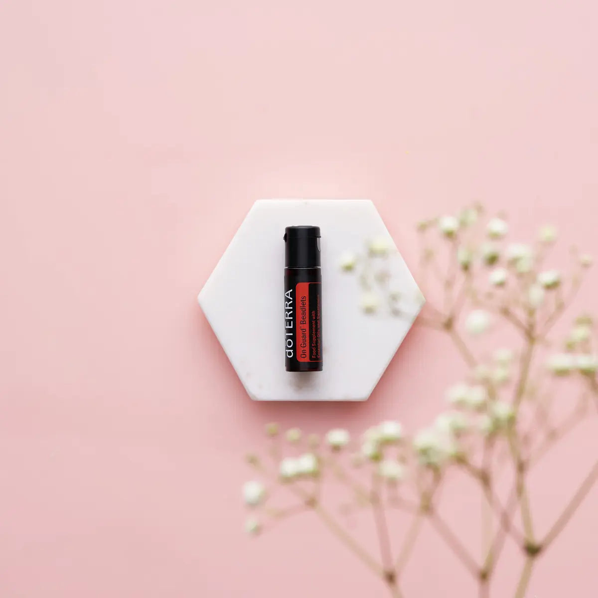 Perlas On Guard dōTERRA — frasco en posavasos hexagonal de mármol con gypsophila, flores blancas y rosas
