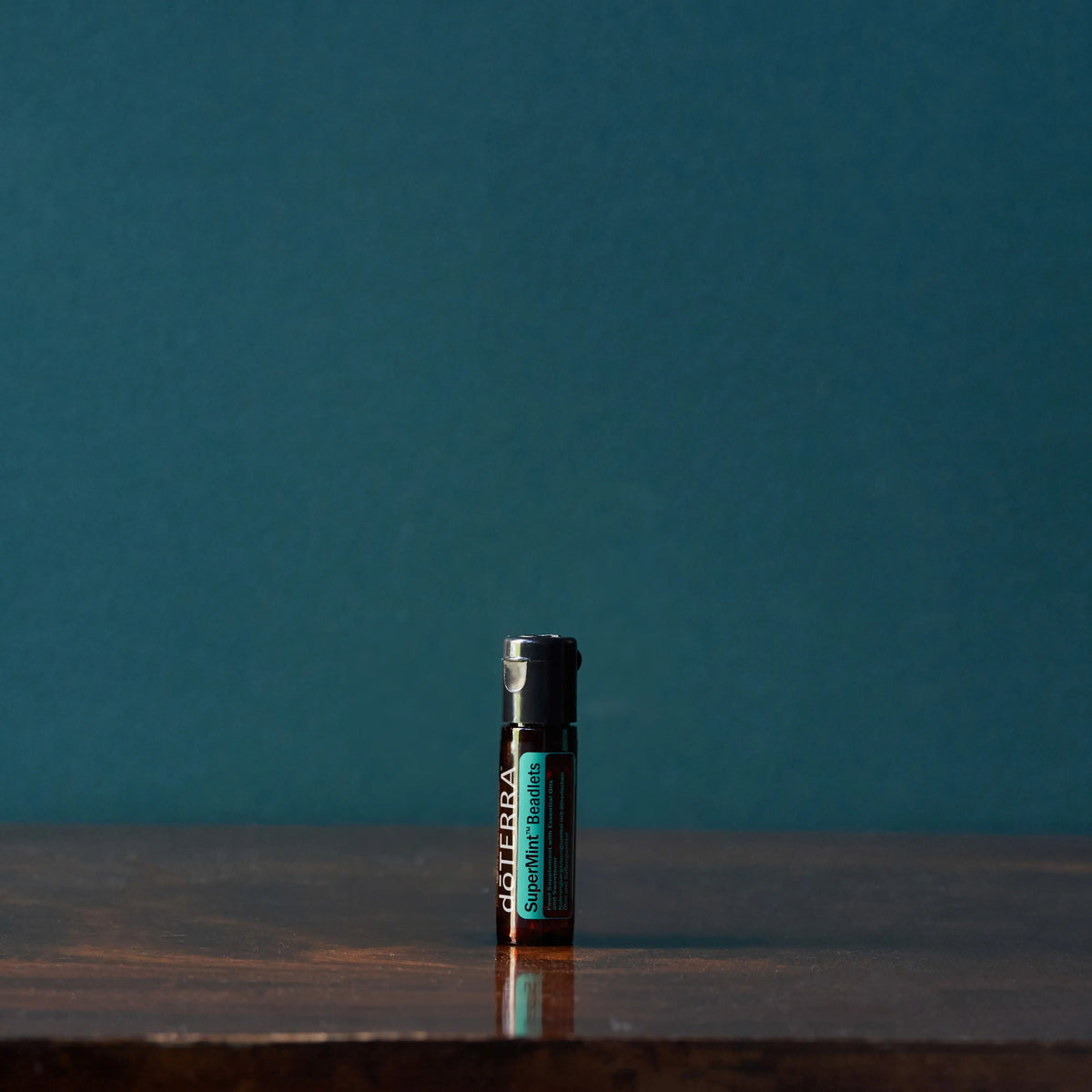 Perlas Supermint dōTERRA — frasco sobre mesa de madera oscura con fondo verde azulado en estudio