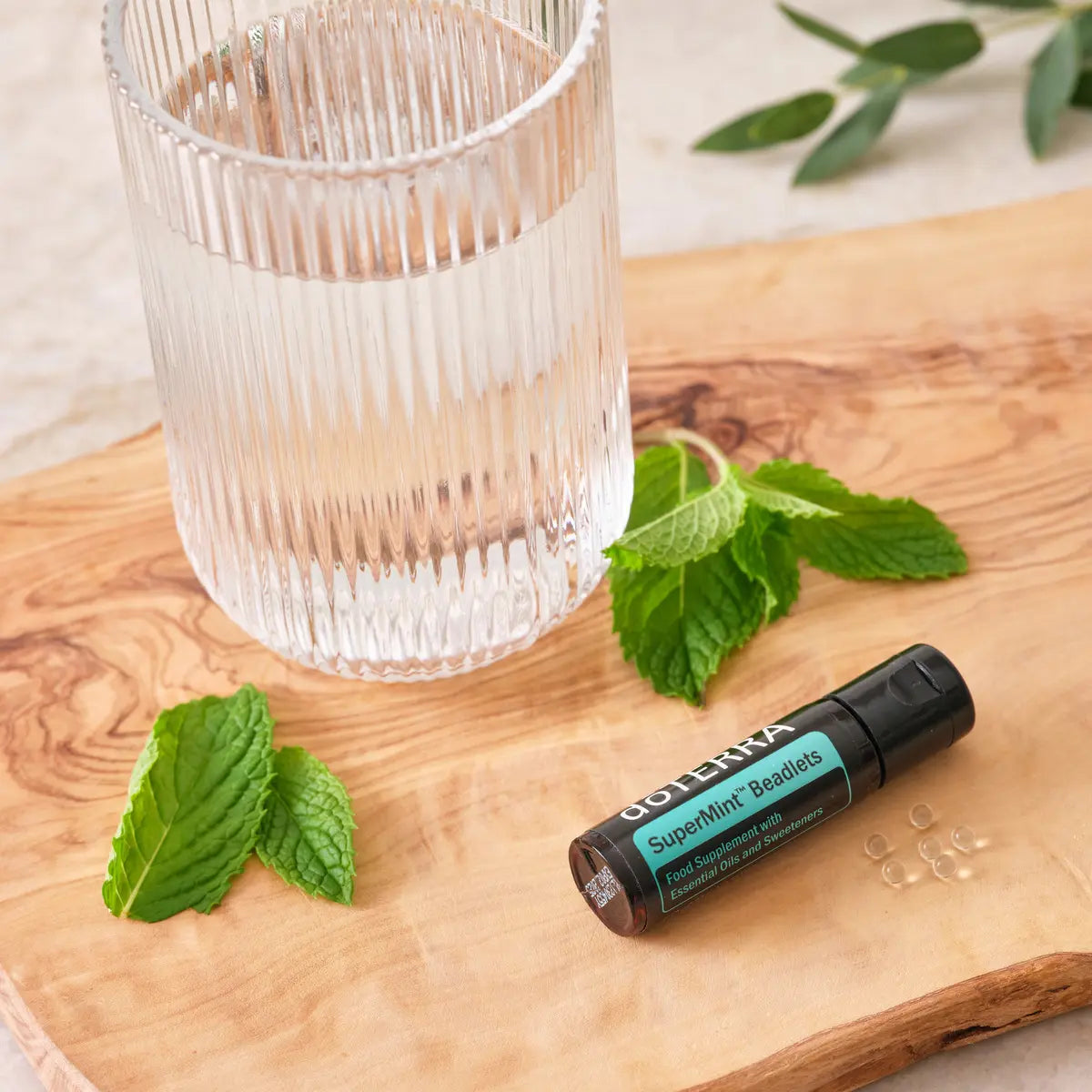Perlas Supermint dōTERRA — frasco en tabla de madera de olivo con vaso de agua y hojas de menta