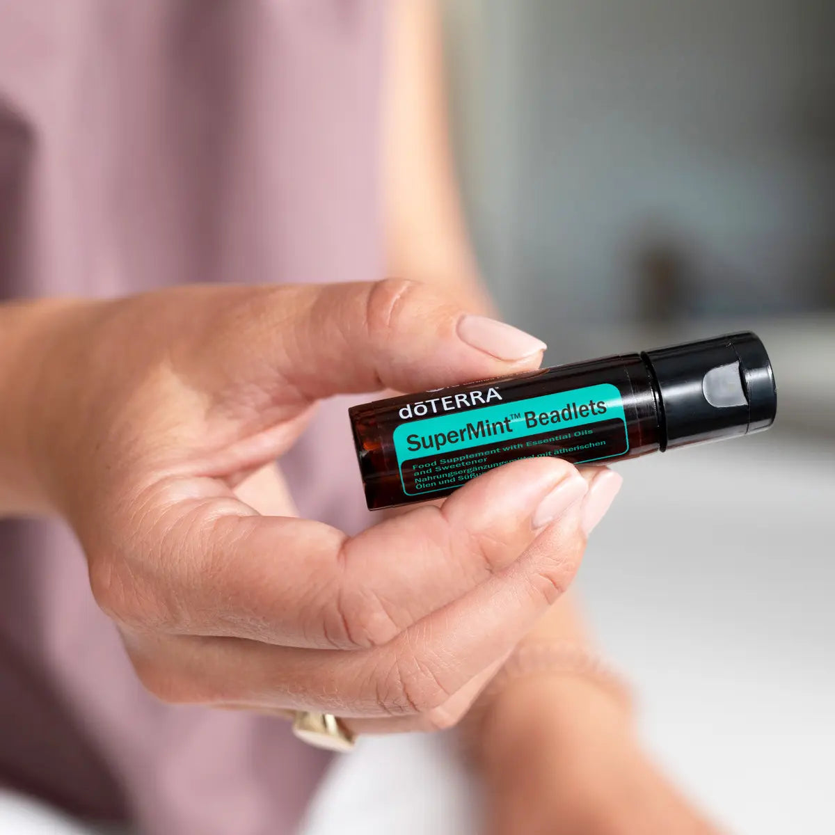Perlas Supermint dōTERRA — mano sosteniendo el frasco en horizontal en primer plano con bokeh violeta