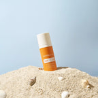 Protector solar Sun Face dōTERRA SPF 30 — frasco en arena con conchas y fondo azul
