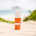 Protector solar Sun Face dōTERRA SPF 30 — frasco en arena de playa con mar e isla al fondo