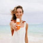 Protector solar Sun Face dōTERRA SPF 30 — mujer sosteniendo cámara en la playa con viento