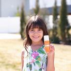 Protector solar Sun Face dōTERRA SPF 30 — niña morena sonriente aplicando en el exterior del jardín