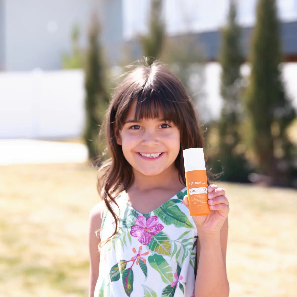 Protector solar Sun Face dōTERRA SPF 30 — niña morena sonriente aplicando en el exterior del jardín
