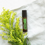 Árbol de Té Touch dōTERRA 10ml con flores de solidago amarillas sobre tela de lino blanco cenital