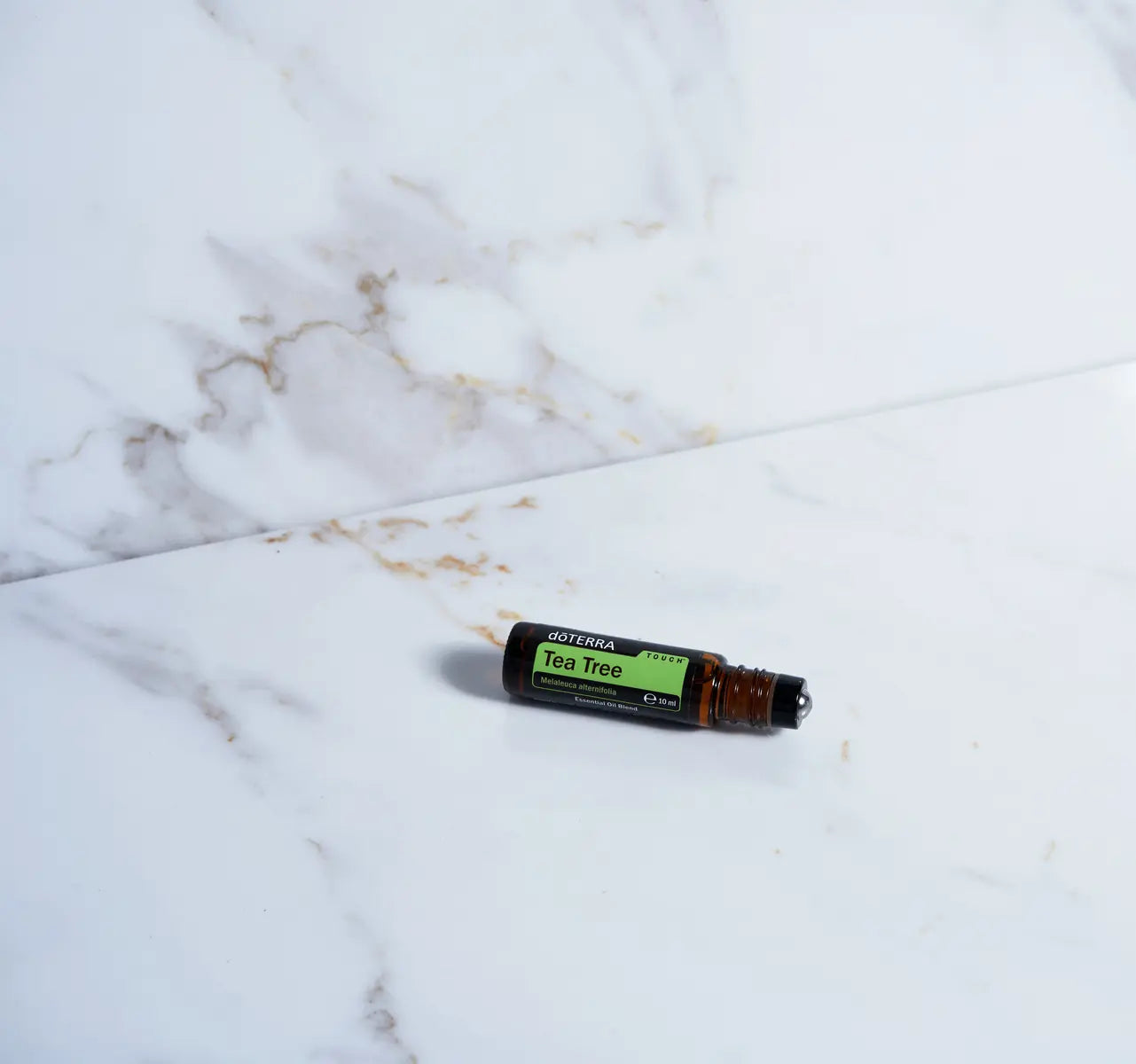 Árbol de Té Touch dōTERRA 10ml tumbado sobre mármol blanco y dorado