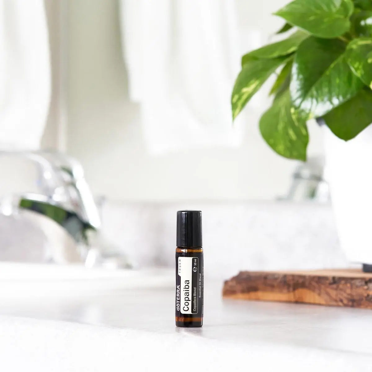 Aceite Esencial Copaiba Touch dōTERRA roll-on 10ml sobre encimera de baño junto al grifo y planta pothos