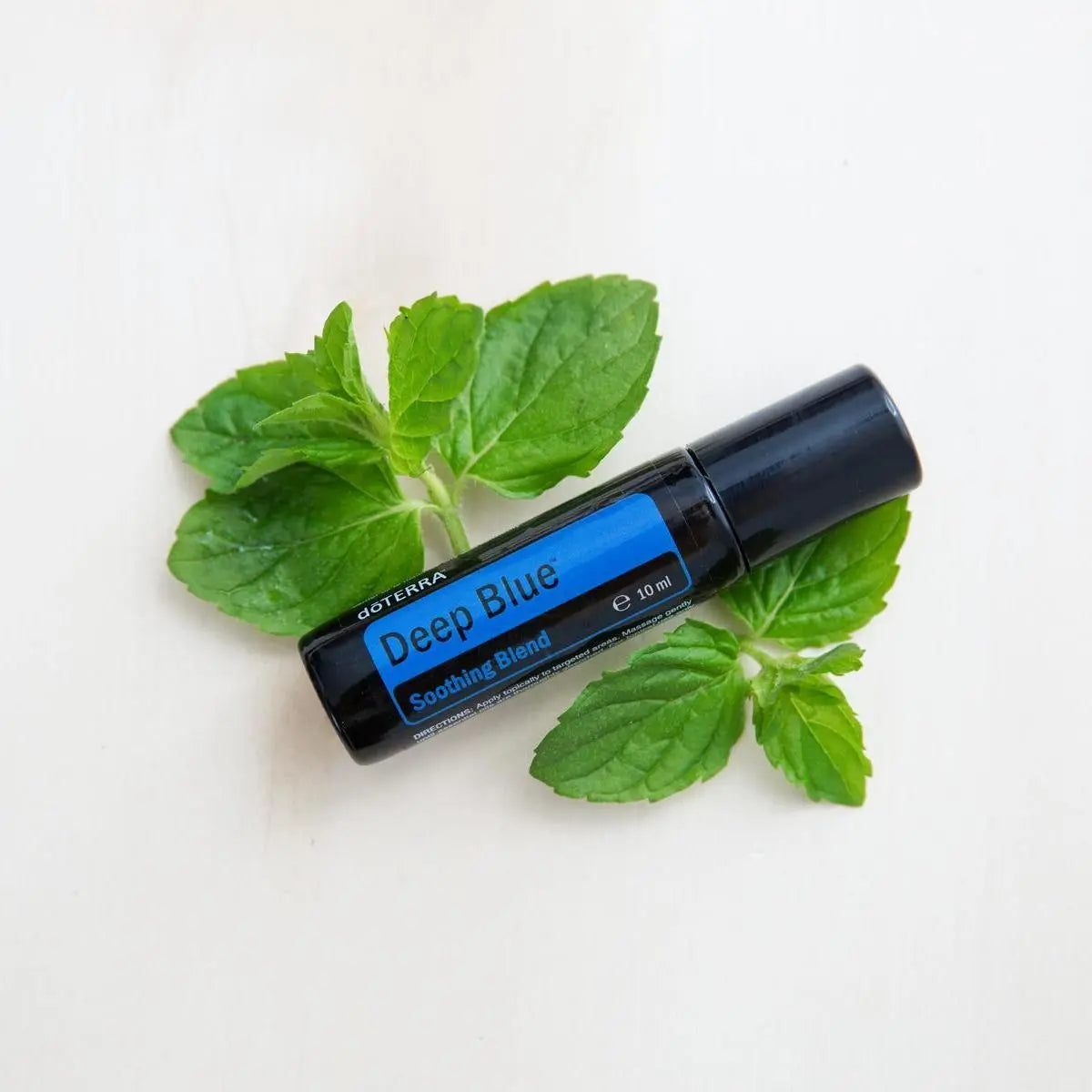 Roll-on dōTERRA Deep Blue 10ml — sobre hojas de menta fresca en superficie blanca, vista cenital