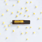 Roll-on Helichrysum Touch dōTERRA 10ml — frasco sobre plato cerámico con flores blancas
