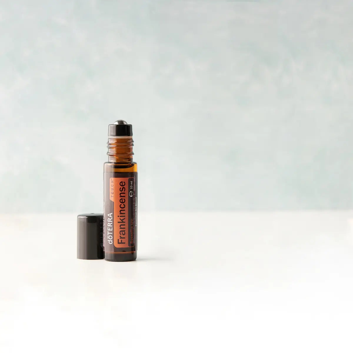 Frankincense Incienso Touch dōTERRA roll-on 10ml con tapa a un lado sobre fondo gris azulado