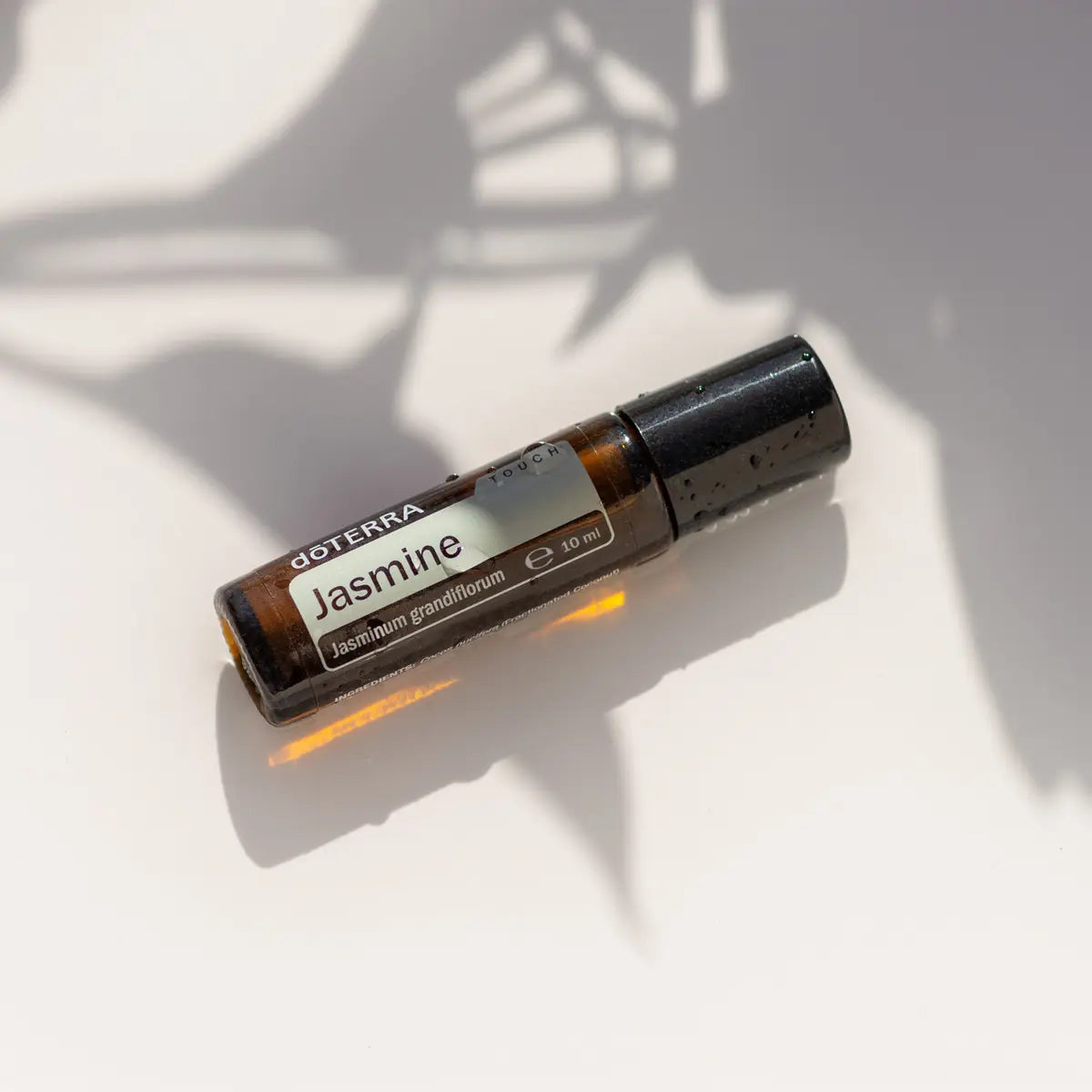 Jazmín Touch dōTERRA 10ml sobre superficie blanca con sombras de hojas naturales