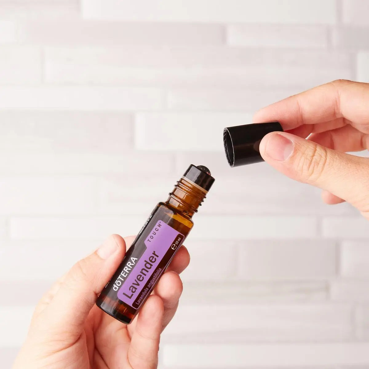 Manos abriendo Lavanda Touch dōTERRA 10ml junto a pared de azulejo blanco