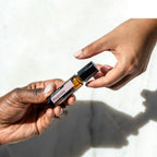 Dos manos pasándose Magnolia Touch dōTERRA 10ml con luz solar y sombras naturales