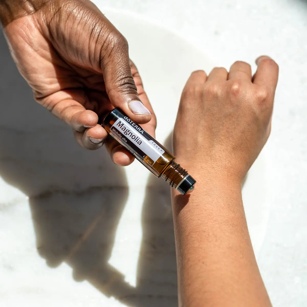 Mano de piel oscura aplicando Magnolia Touch dōTERRA 10ml en muñeca sobre mármol