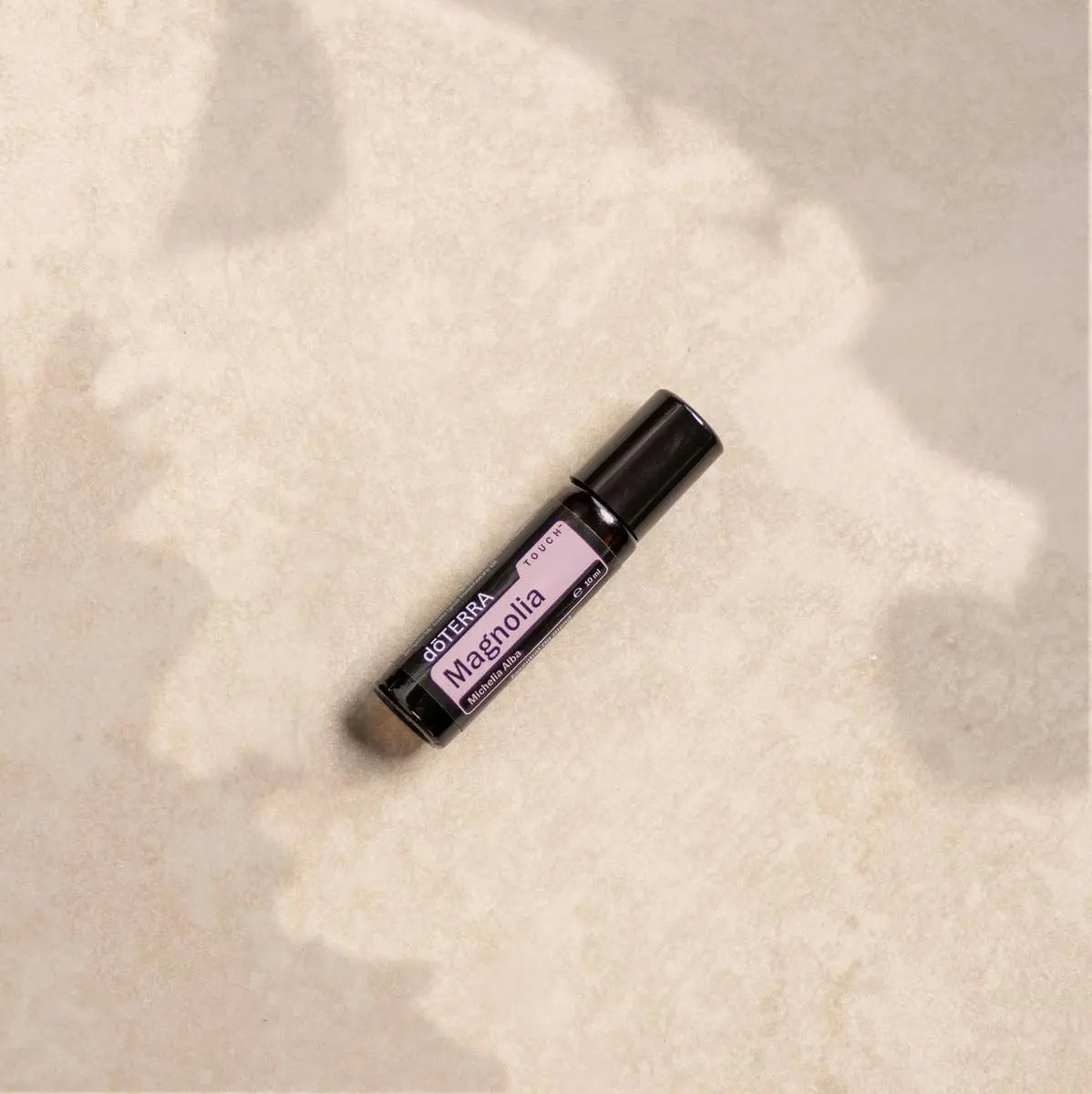 Magnolia Touch dōTERRA 10ml tumbado sobre piedra beige con sombras de hojas
