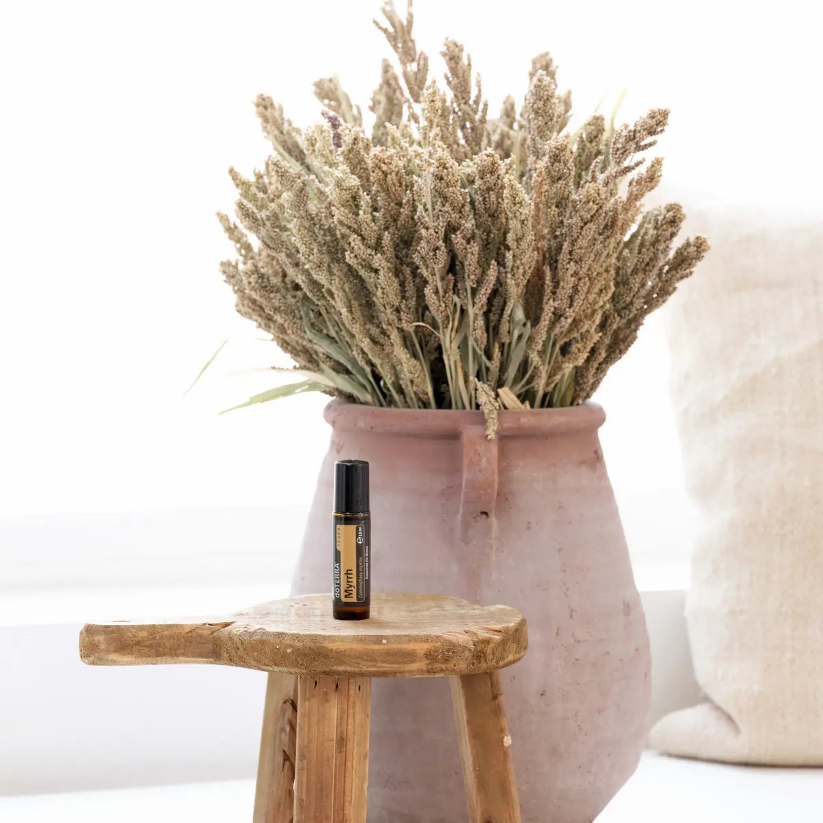 Mirra Touch dōTERRA 10ml sobre taburete de madera rústico con jarrón terracota y plantas secas