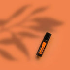 Roll-on Motivate Touch dōTERRA 10ml — frasco sobre fondo naranja con sombras de palmera