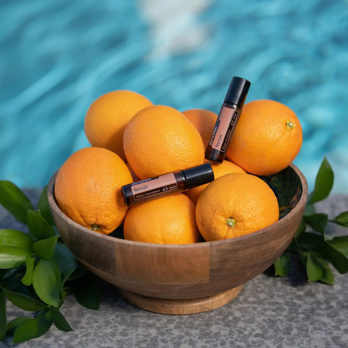 Neroli Touch dōTERRA roll-on 10ml junto a naranjas en cuenco de madera y piscina azul con cítricos