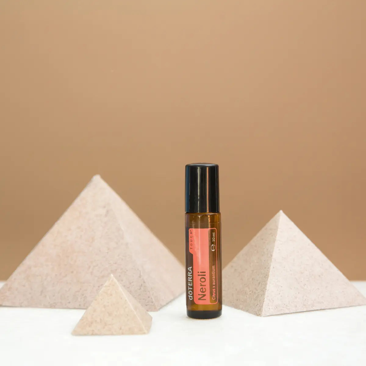 Neroli Touch dōTERRA 10ml junto a pirámides de piedra sobre fondo beige minimalista