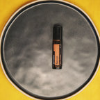 Neroli Touch dōTERRA 10ml en plato de cerámica gris sobre fondo amarillo cenital