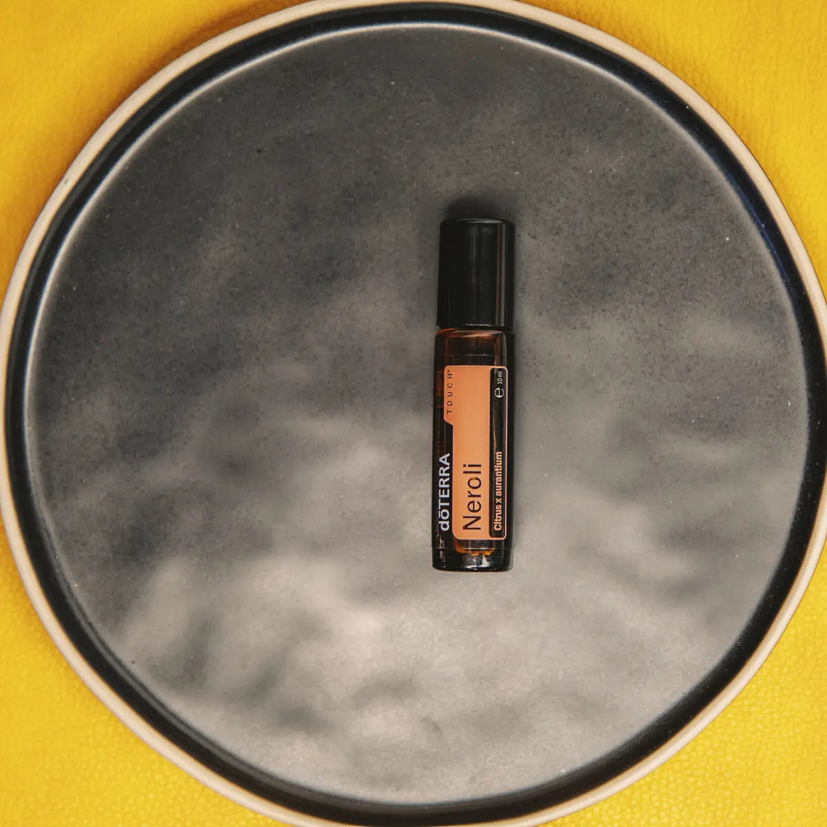 Neroli Touch dōTERRA 10ml en plato de cerámica gris sobre fondo amarillo cenital