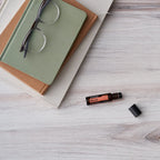 Neroli Touch dōTERRA 10ml tumbado sobre libros y gafas en superficie de madera blanca