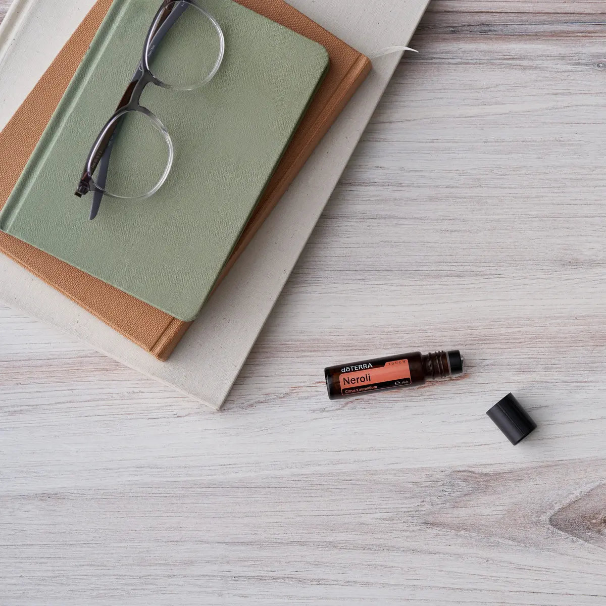 Neroli Touch dōTERRA 10ml tumbado sobre libros y gafas en superficie de madera blanca