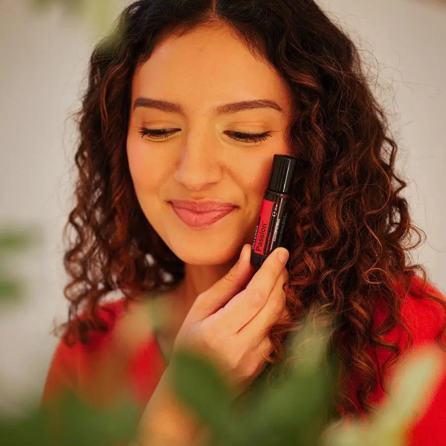 Roll-on Passion Touch dōTERRA 10ml — mujer morena rizada aplicando el roll-on con fondo bokeh