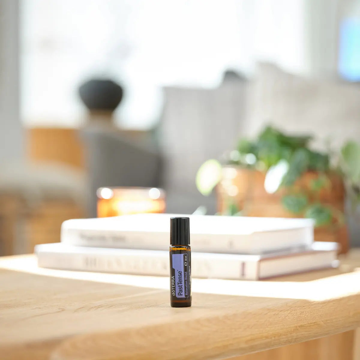 Roll-on PastTense dōTERRA 10ml — frasco sobre mesa de madera con libros y vela en salón