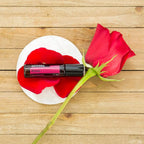 Rosa Touch dōTERRA 10ml en posavasos blanco con rosa roja y pétalos sobre madera cenital