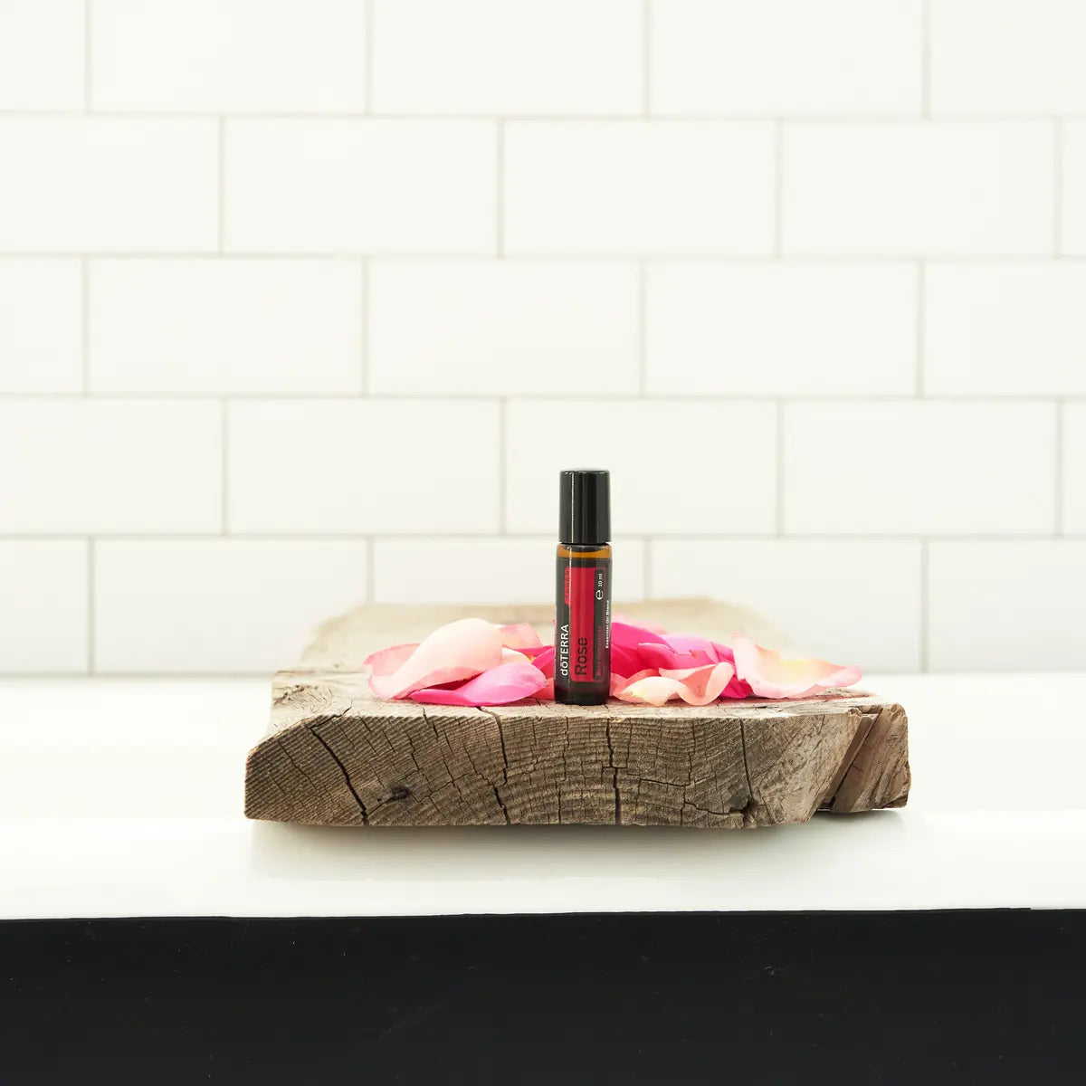 Rosa Touch dōTERRA 10ml sobre tabla de madera rústica con pétalos de rosa y azulejo de baño