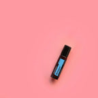 Roll-on Whisper Touch dōTERRA 10ml — frasco inclinado sobre fondo rosa minimalista