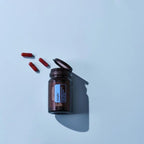 Frasco abierto de Cápsulas Adaptiv dōTERRA con cápsulas rojas sobre fondo azul visto desde arriba