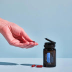 Mano con frasco abierto de Cápsulas Adaptiv dōTERRA sobre fondo azul
