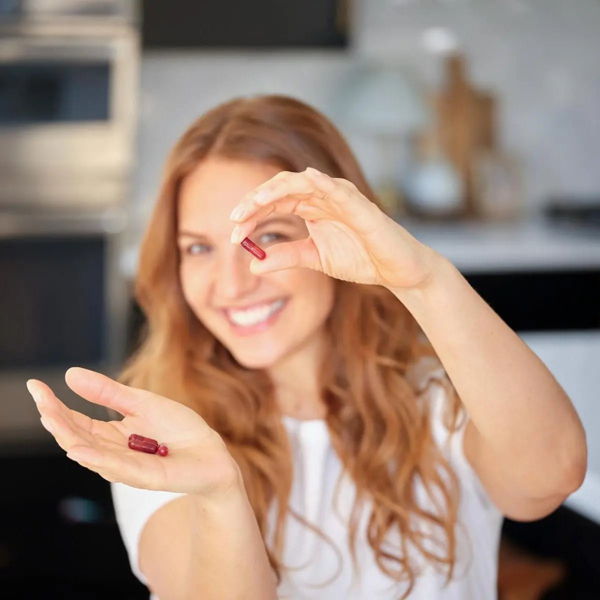 Mujer pelirroja sonriente con cápsula roja de Cápsulas Adaptiv dōTERRA en la cocina