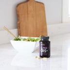 Frasco de Alpha CRS+ dōTERRA junto a ensalada verde sobre mármol y tabla de madera