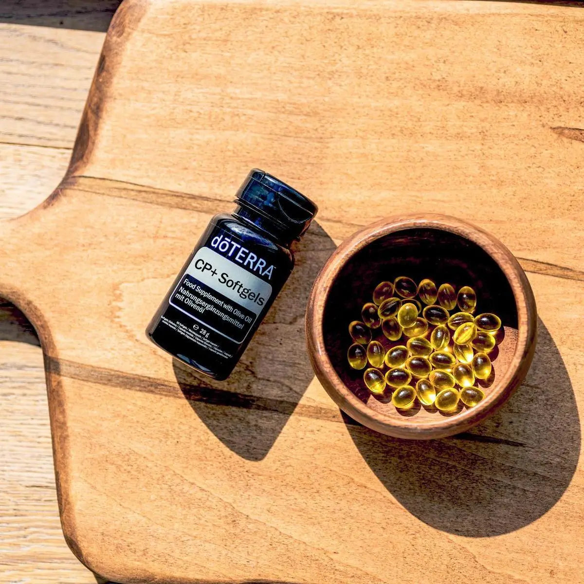 Frasco de Cápsulas Blandas CP+ dōTERRA con cuenco de madera y softgels sobre tabla visto desde arriba
