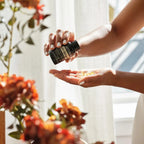 Manos sosteniendo frasco de Cápsulas Blandas CP+ dōTERRA con flores naranjas