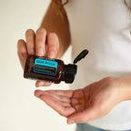 Manos con frasco abierto de DDR Prime Softgels dōTERRA y softgel en la palma