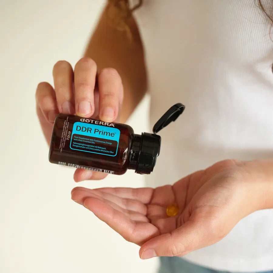 Manos con frasco abierto de DDR Prime Softgels dōTERRA y softgel en la palma
